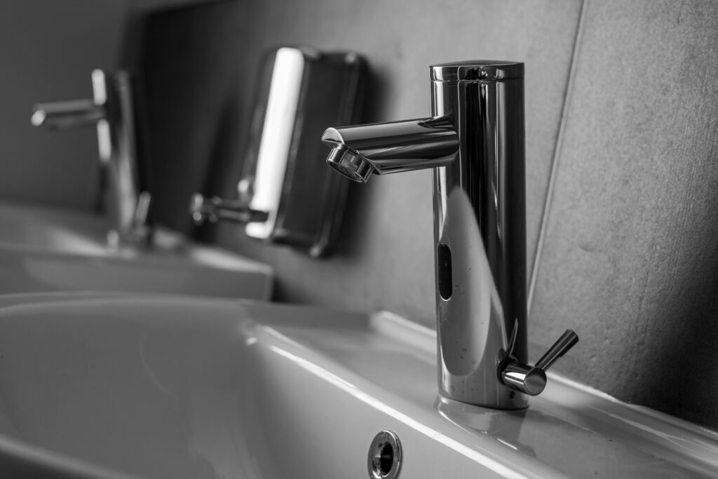 Close-up of a sleek stainless steel faucet over a white sink in grayscale.
