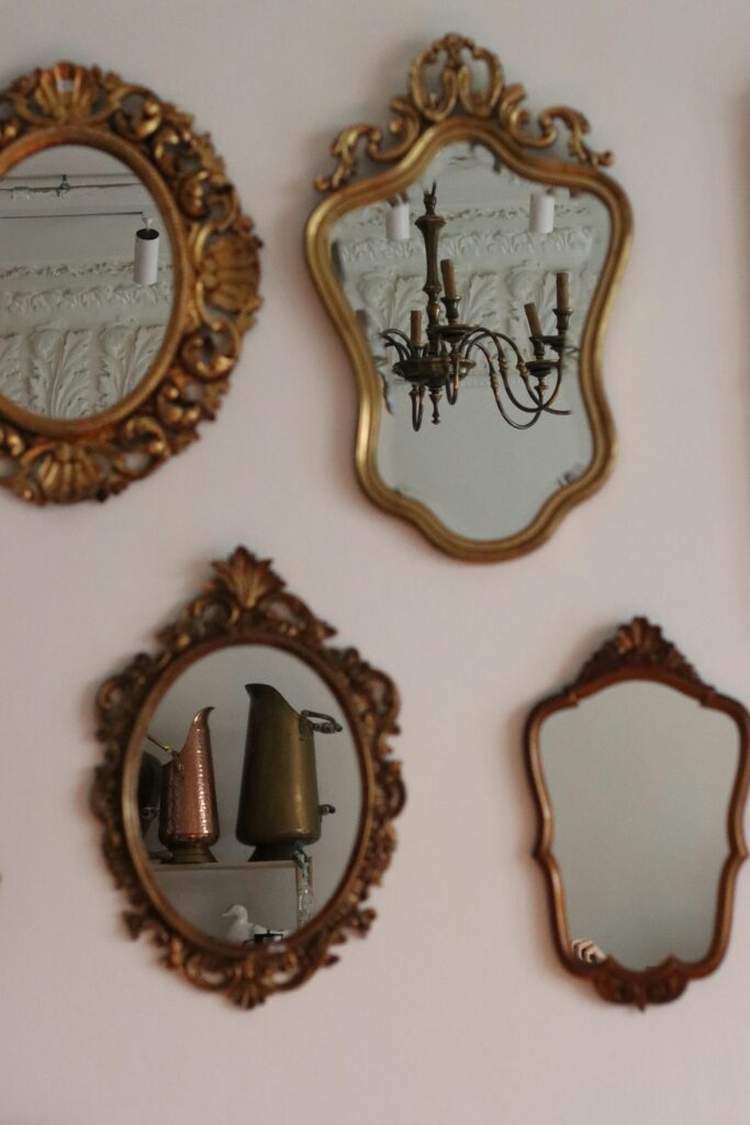 Collection of vintage ornate mirrors on a wall reflecting a chandelier and vases.
