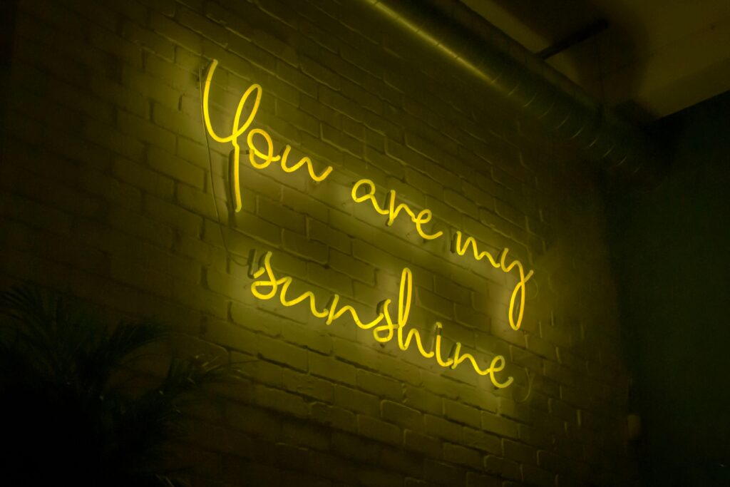 From below of illuminated signboard You are my sunshine with yellow neon light on white wall in dark room