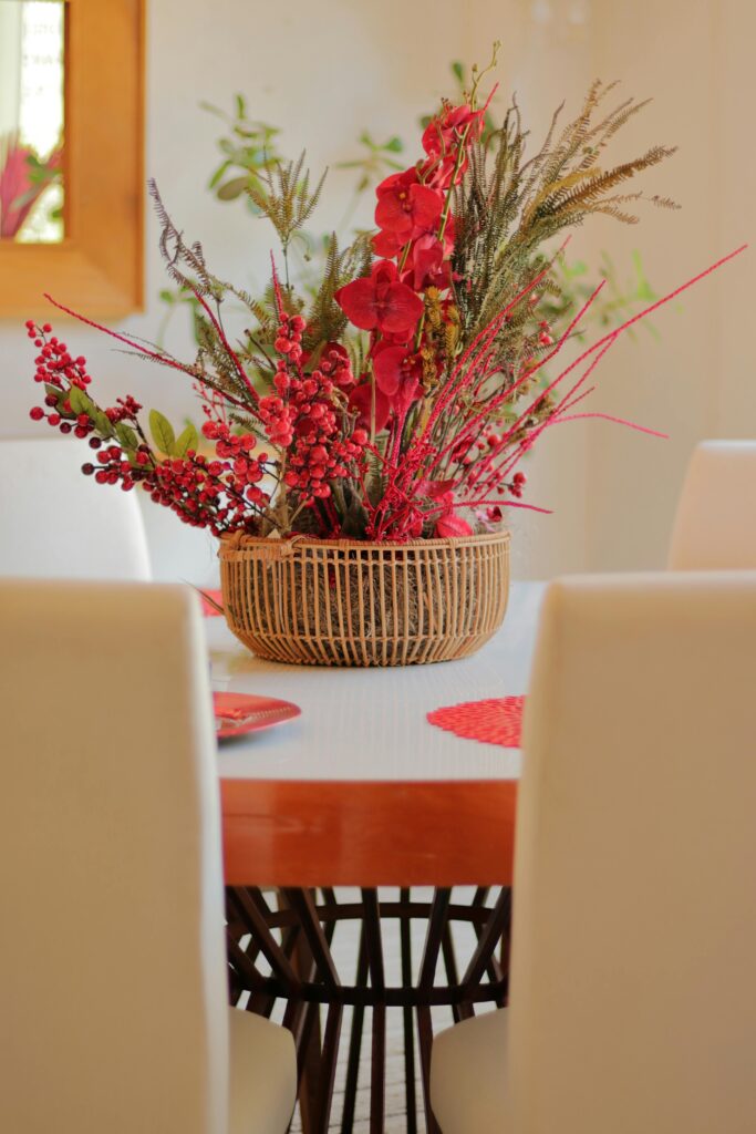 Stylish red and green floral arrangement in wicker basket on modern dining table.
