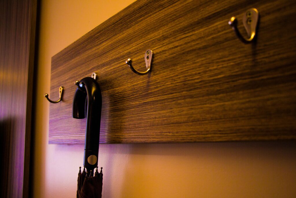 A close-up of a wooden hook board indoors with an umbrella hanging, showcasing a modern design.
