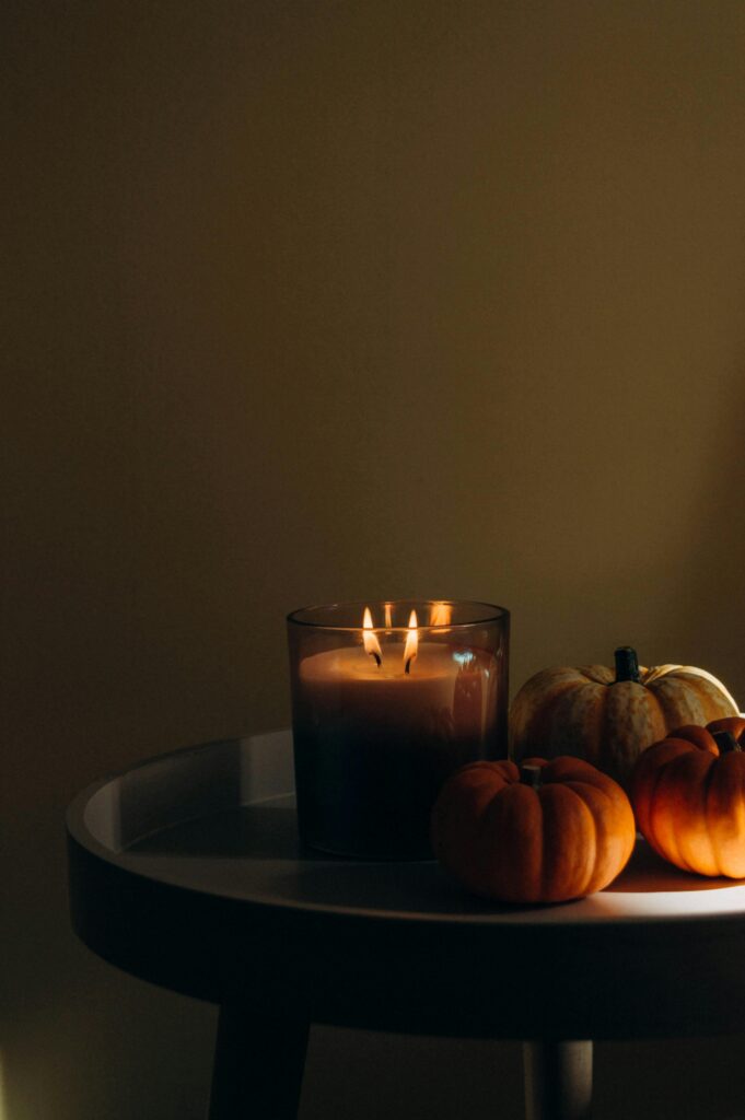 Warm candlelight with small pumpkins on a table creates a cozy autumn atmosphere.