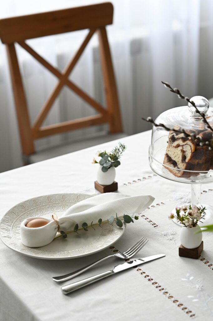 A sophisticated table setup featuring a decorated egg, a plate of pastries, and floral accents for a refined dining experience.