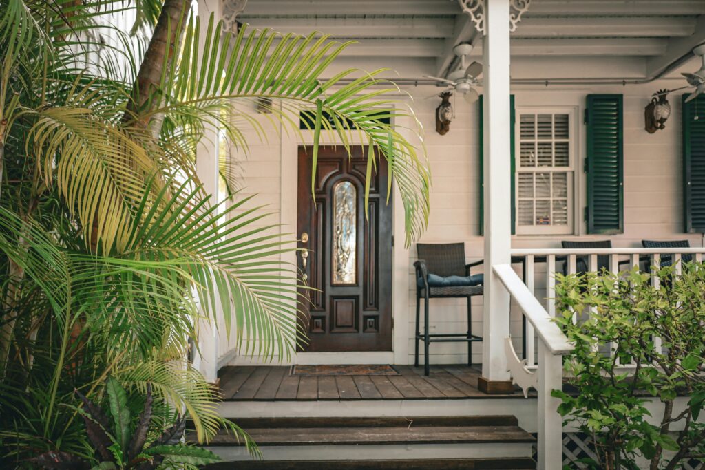 Colonial house entrance with tropical plants and wooden door, ideal for architecture lovers.
