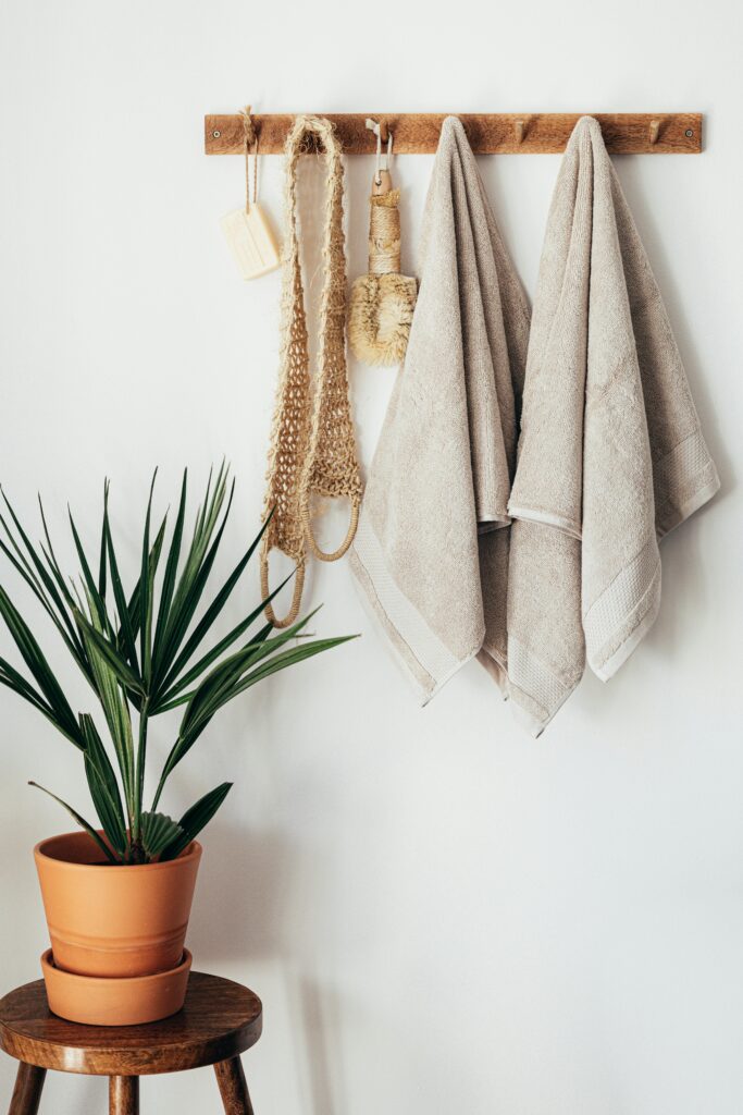 Stylish bathroom interior with houseplant on wooden table against white wall with hanging towels and set of eco friendly body care items
