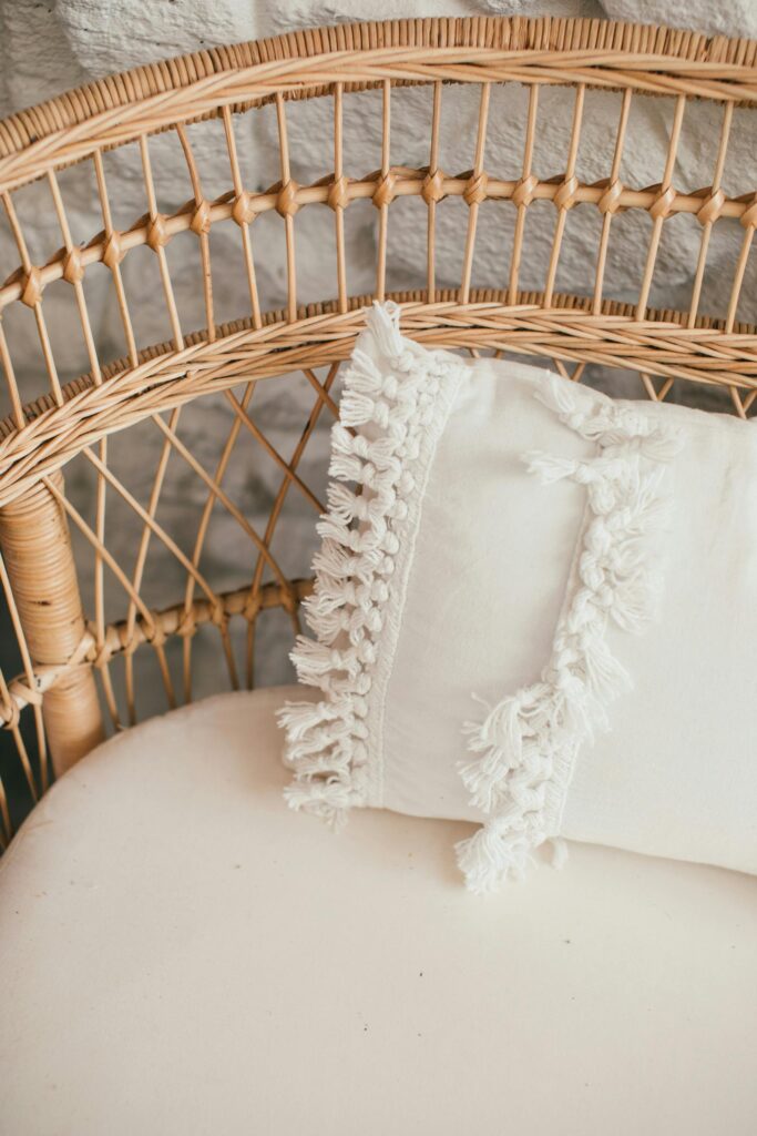Stylish wicker chair with a decorative pillow featuring fringe details, ideal for cozy interiors.