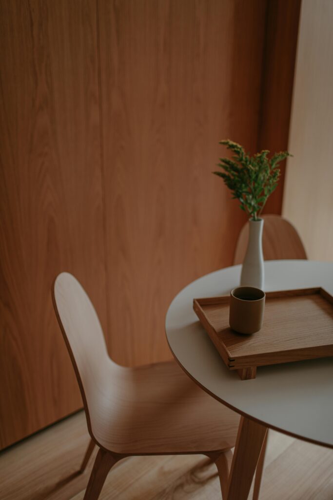 Stylish minimalist dining setting with wooden features, a tray, and a vase on a round table.