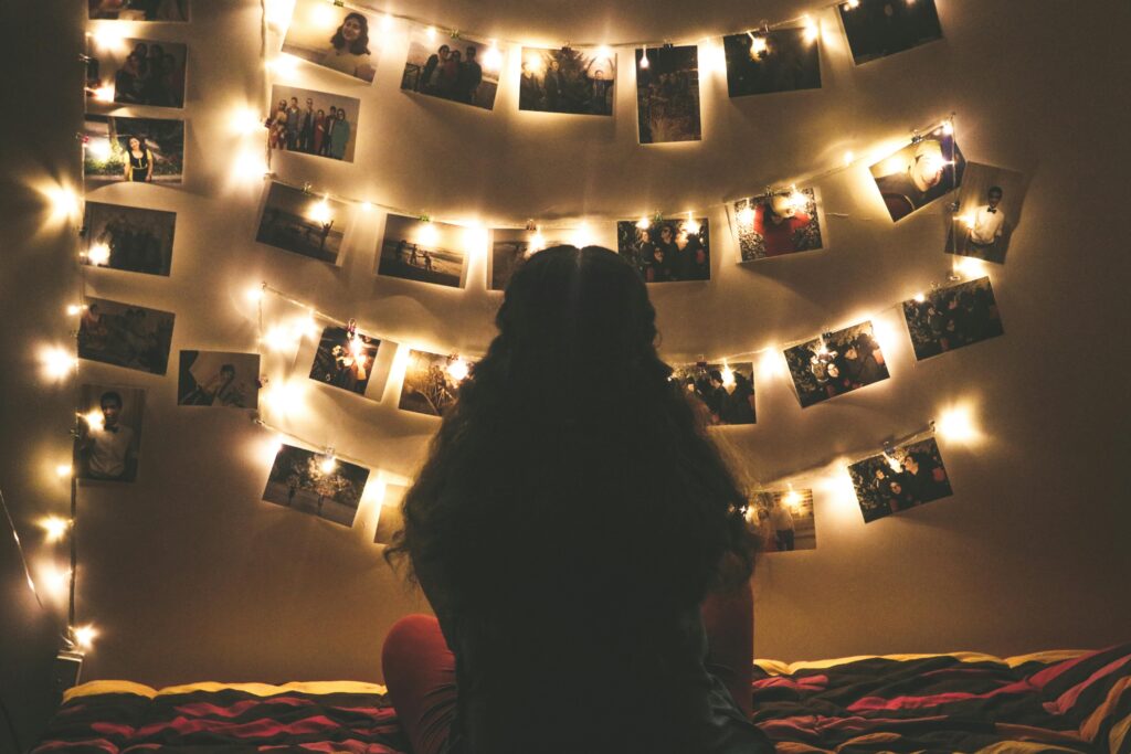 A warmly lit bedroom featuring string lights and a woman viewing hanging photos.